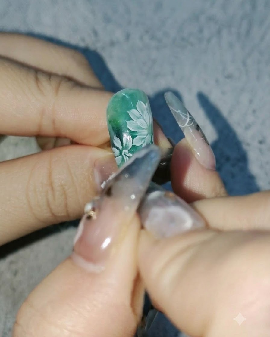 Nahaufnahme einer Nageldesignerin, die tiefere weiße Blütenblätter zu Gänseblümchen auf einem grünen Nageldesign hinzufügt.