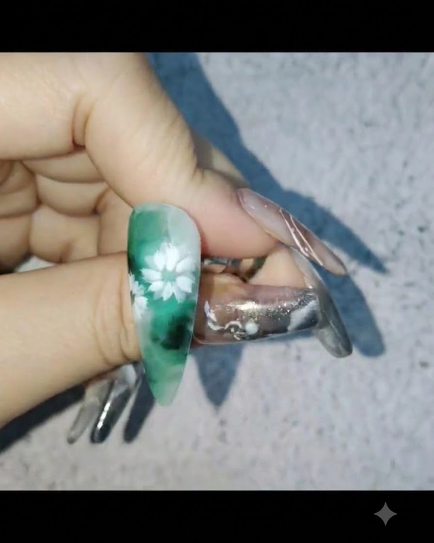 Eine Hand hält einen Nagel mit weißer Gänseblümchen-Nail-Art, während eine schützende Schicht Verstärkungsgel aufgetragen wird.