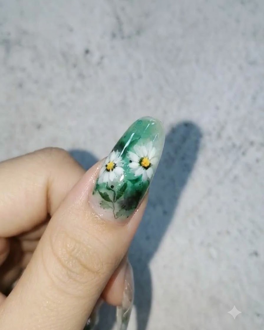 Ein fertiges Nageldesign mit weißen Gänseblümchen und Blättern auf einem grünen Hintergrund mit glänzenden 3D-Wassertropfen auf der Oberfläche.