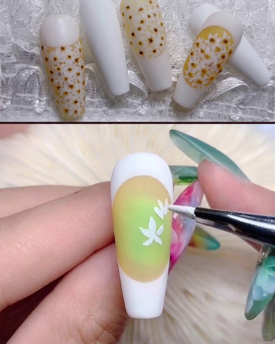 Ein feiner Pinsel malt weiße Gänseblümchen-Blütenblätter auf den gelblich getönten Nagel.