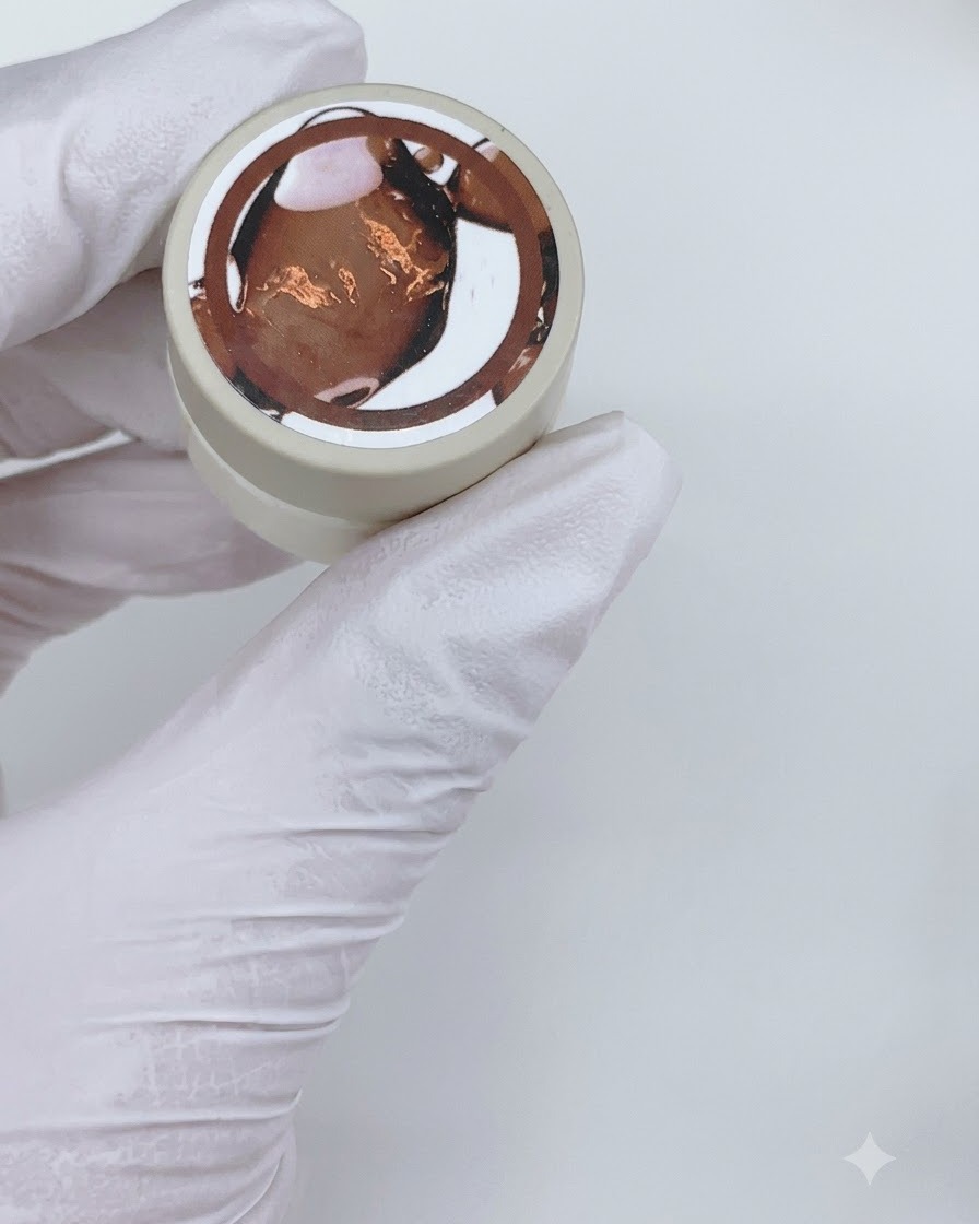 Ein flacher Gelpinsel trägt eine Schicht transparentes braunes Gel-Nagellack auf einen transparenten Nagel-Display-Stick auf.