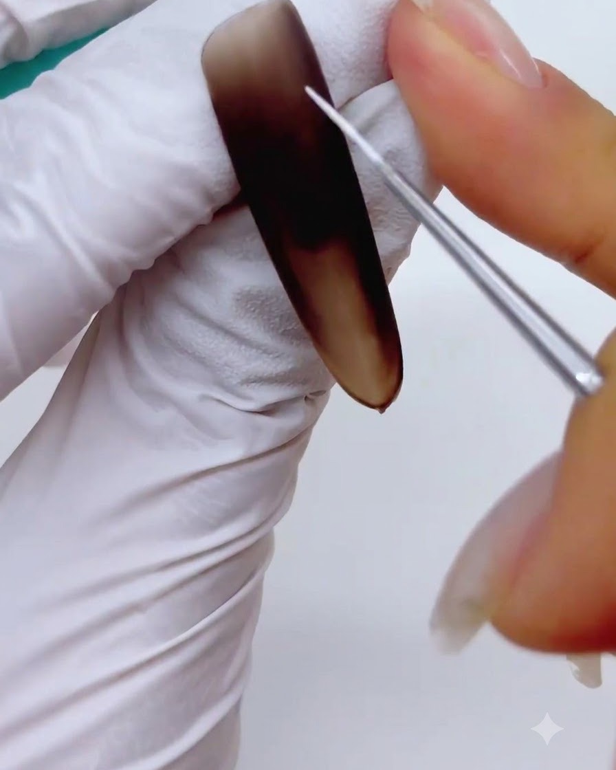 Nahaufnahme eines feinen Liner-Nail-Art-Pinsels, der dünne, sich kreuzende weiße Linien malt, um ein Schneeflocken-Skelett auf einem matten braunen Nagel zu bilden.