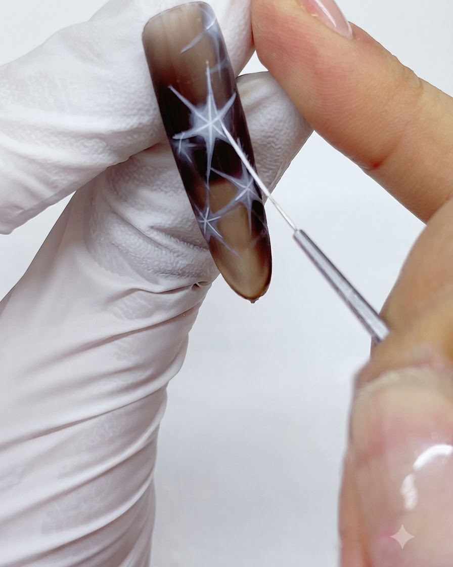 Ein feiner Liner-Pinsel zieht und umrandet sorgfältig die äußeren Ränder eines weißen Stern-Designs auf einem Nagel.