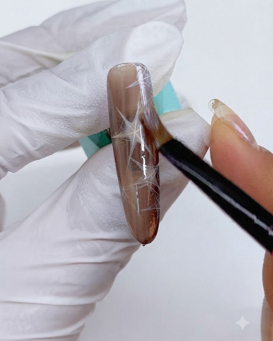Ein feiner Pinsel trägt Cat-Eye-Gel über den verzierten braunen Nagel auf.