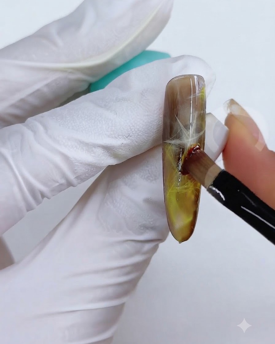 Eine Pinsel- und Schwammtechnik wird verwendet, um die gelb-braune Farbe auf der Nageloberfläche zu verblenden.