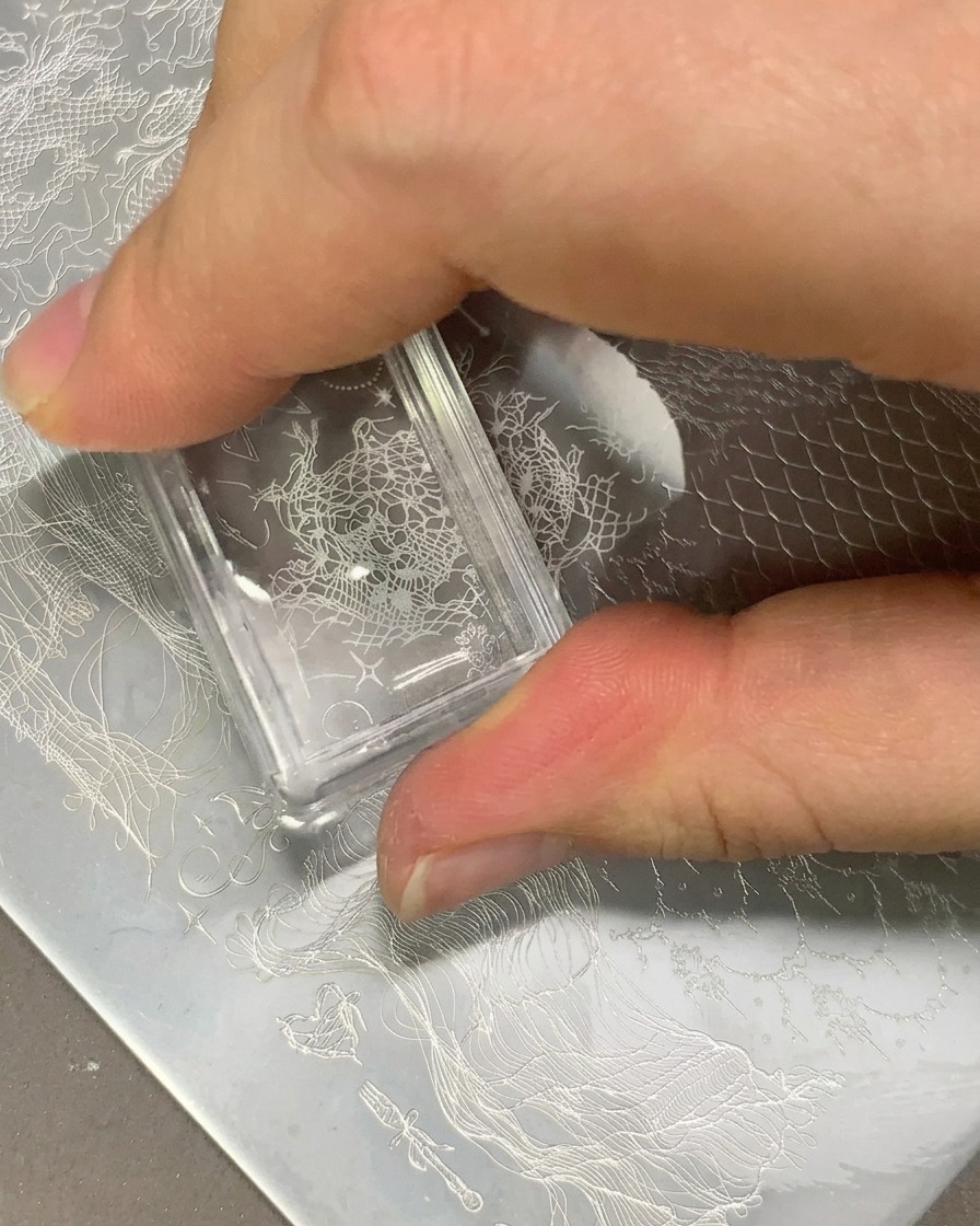 Ein klarer Stamper überträgt ein weißes Spitzenmuster auf eine klare Nagelspitze.