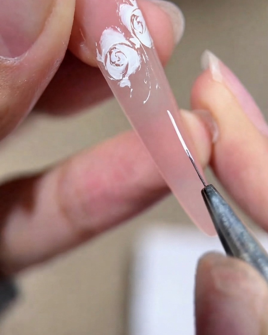 Nahaufnahme einer Nageldesignerin, die eine weiße Klammerform auf eine rosa Nagelplatte zeichnet.