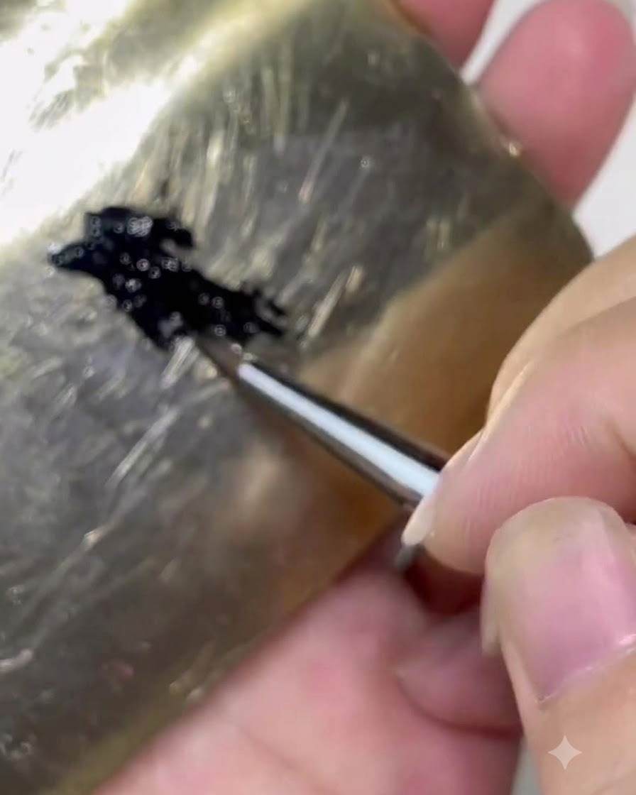 Ein Pinsel, der schwarzes Gelprodukt von einer Palette auf etwa ein Drittel des Pinselhaars aufnimmt.