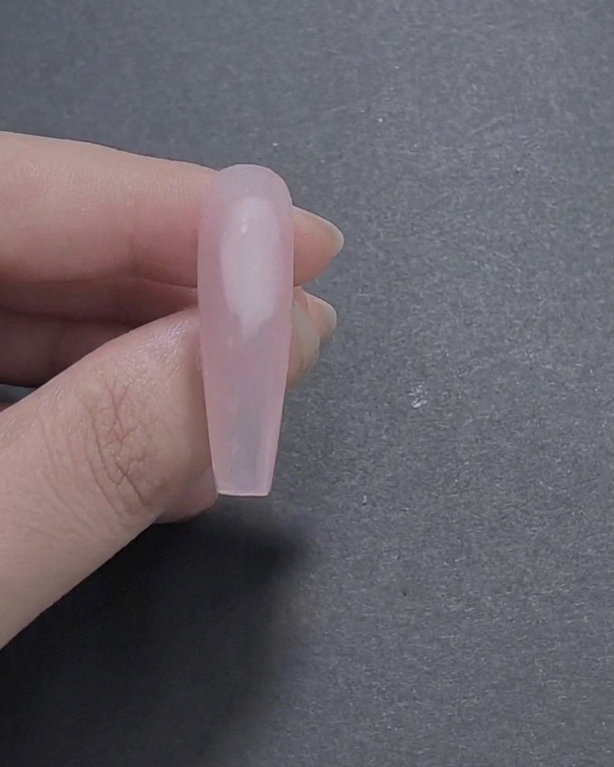 Eine Nahaufnahme eines langen sargförmigen Nagels mit einer glatten, glänzenden zartrosa Gel-Basis, die zwischen Fingern gehalten wird.
