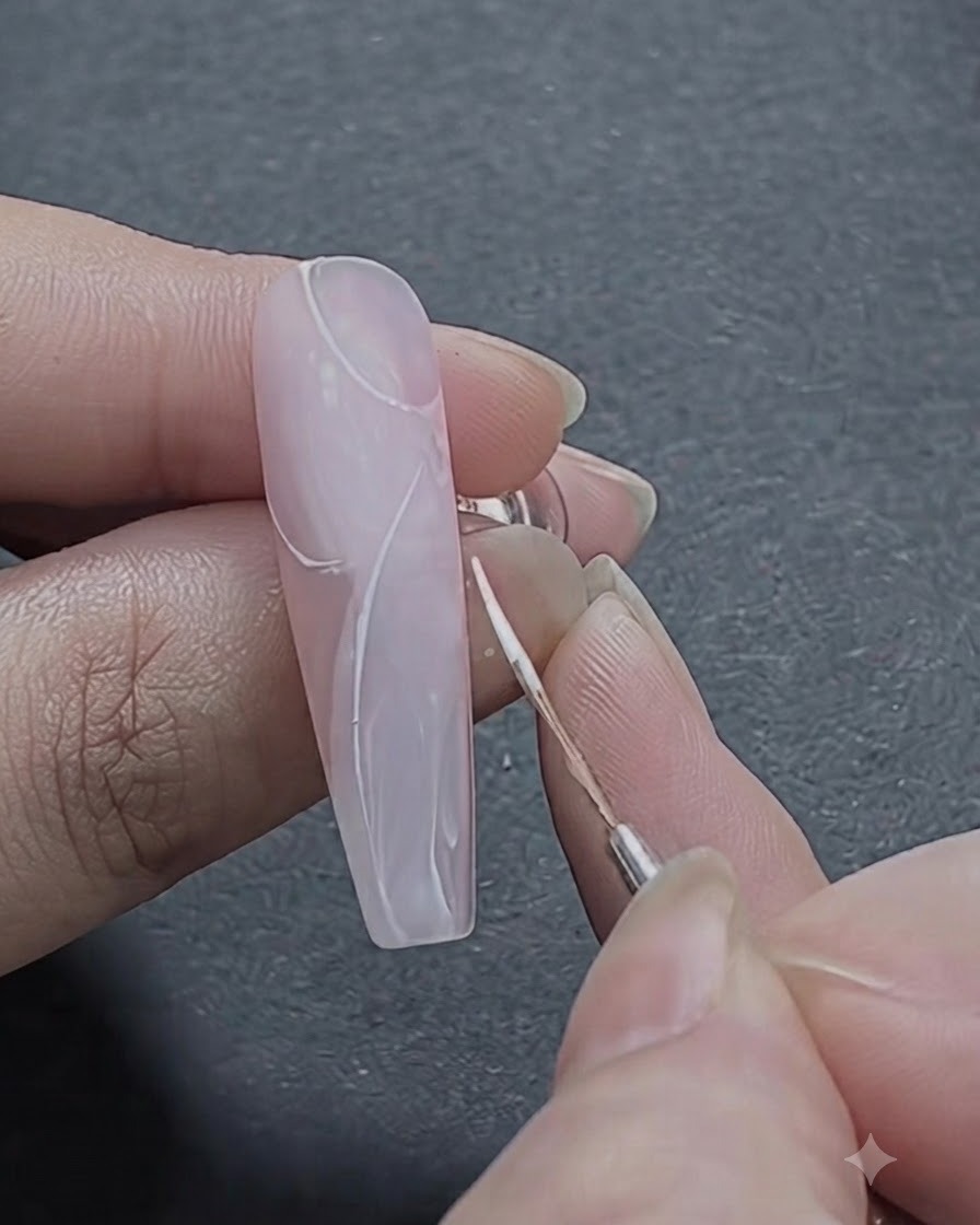 Ein feiner Pinsel skizziert die ersten geschwungenen weißen Striche eines Rosenmusters im oberen Nagelbereich.