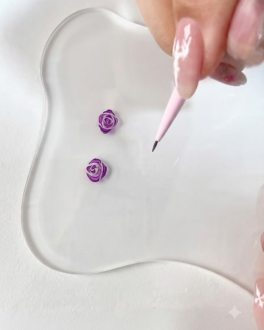 Eine Nahaufnahme eines feinen Pinselstrichs, der ein kleines, geschwungenes lila Blütenblatthäkchen auf einer transparenten Palette zeichnet.