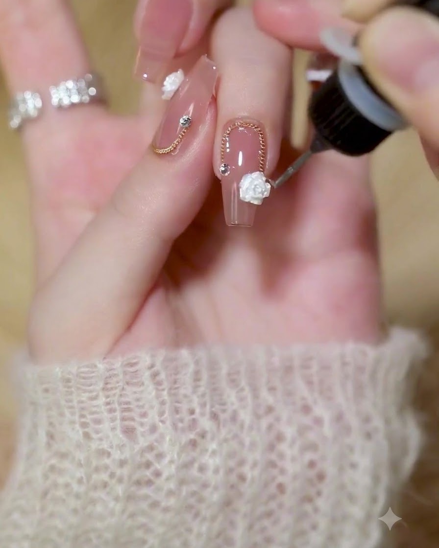 Ein feiner Detailpinsel trägt klaren Builder Gel um die Ränder einer weißen 3D-Rose und Goldkette auf einen polierten Nagel auf.