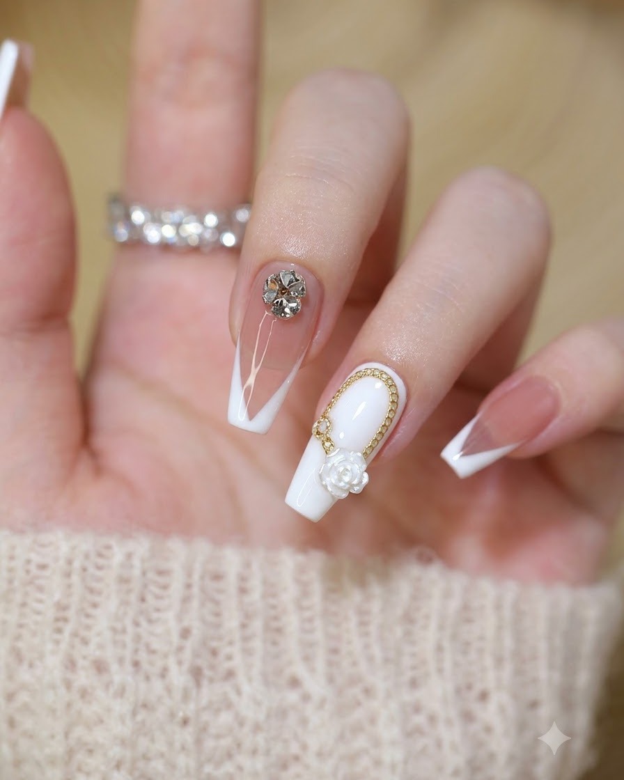 Nahaufnahme eines fertigen Sets von Feen-Nägeln mit weißen Rosen, Goldketten und Kristall-Strasssteinen.