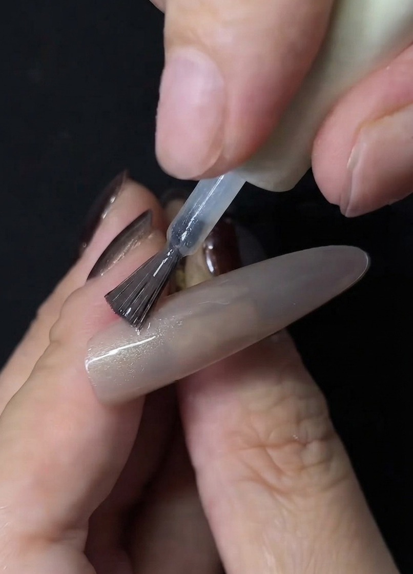 Ein Magnetstab bündelt die Partikel im klaren Cat-Eye-Gel auf einer Nude-Nagelverlängerung zu einem Glasperlen-Effekt.