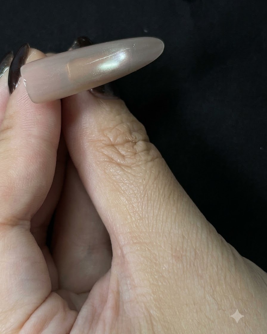 Eine fertige, lange Nude-Cat-Eye-Nagelverlängerung vor einem dunklen Hintergrund, die eine sanft reflektierende Mittellinie zeigt.