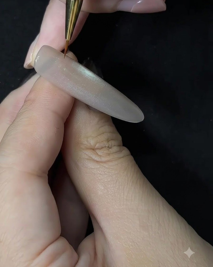 Nahaufnahme einer Nail-Artistin, die mit einem feinen Detailpinsel weißes Gel in Tupfbewegungen auf eine modellierte Nagelverlängerung aufträgt.