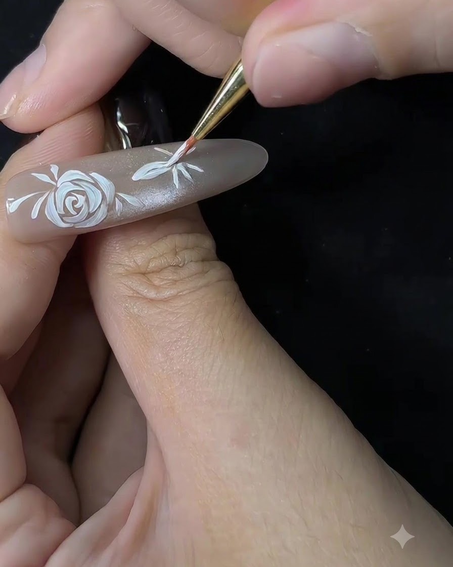Nahaufnahme eines feinen Pinsels, der beginnt, die Blütenblätter einer zweiten Blume auf einer nudefarbenen Nagelverlängerung zu formen.