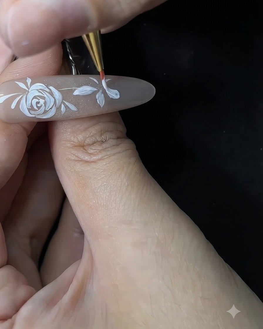 Eine Nageldesignerin verfeinert und verdickt mit einem feinen Pinsel die weißen Blütenblätter einer kleinen Blume auf einer Gelnagel-Verlängerung.