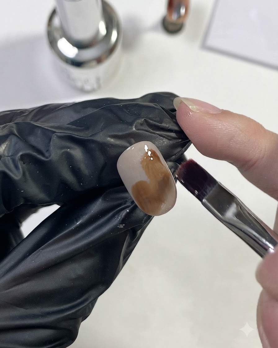 Ein Nagelpinsel trägt helles Karamellbraun-Gel in einem großen Fleck auf den Nagel auf.