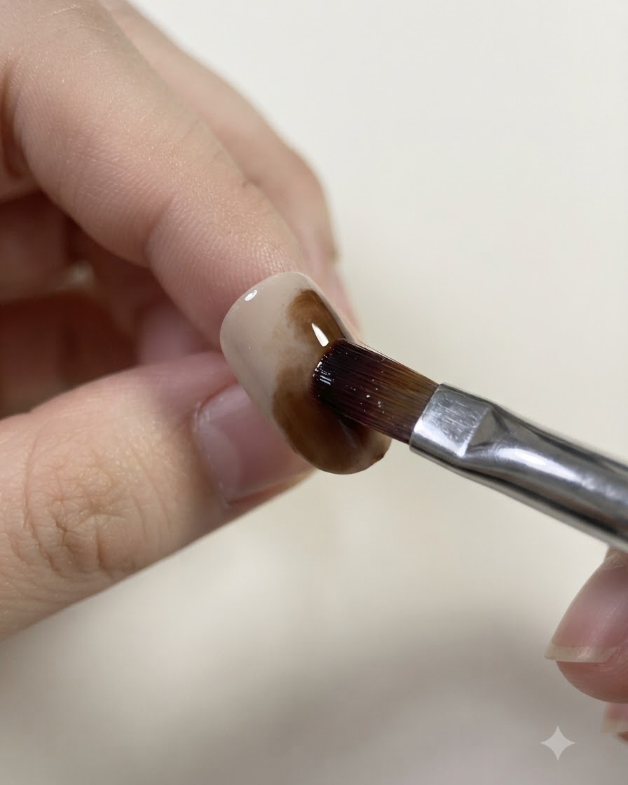 Ein angefeuchteter Pinsel verblendet und weicht die Ränder des Karamell-Gels auf einem Nagel auf.