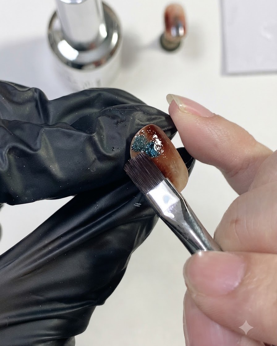 Ein Nagelpinsel platziert einen kleinen Tupfer glitzernden blauen Magnet-Cat-Eye-Gels auf die Seite des Bernsteinnagels.