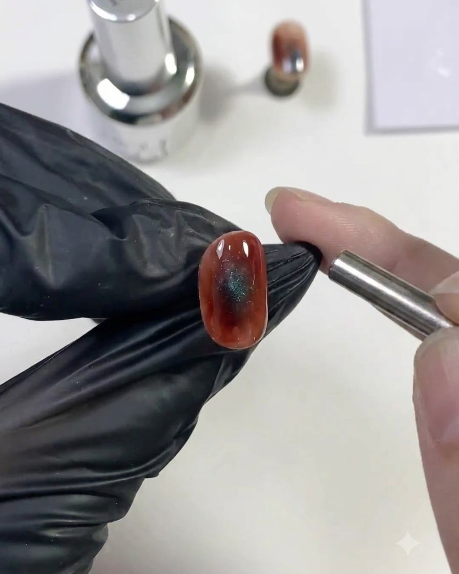 Ein zylindrischer Magnet wird nahe an ein feuchtes blaues Cat-Eye-Nageldesign gehalten, um die glitzernde Lichtreflexion zu ziehen.