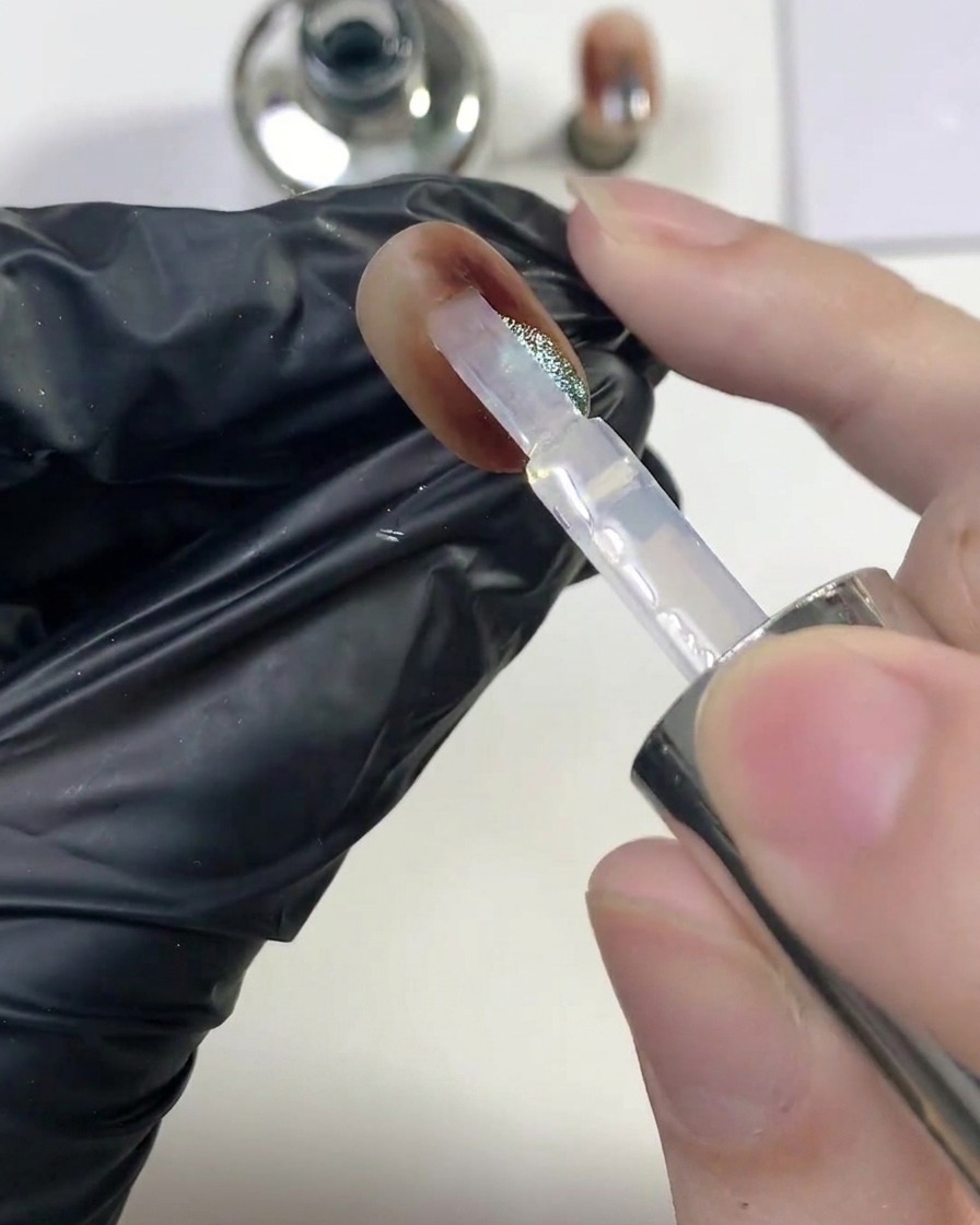 Ein Pinsel lässt eine großzügige Schicht klaren Glanz-Top-Coats über den fertigen Bernstein-Cat-Eye-Nagel gleiten.