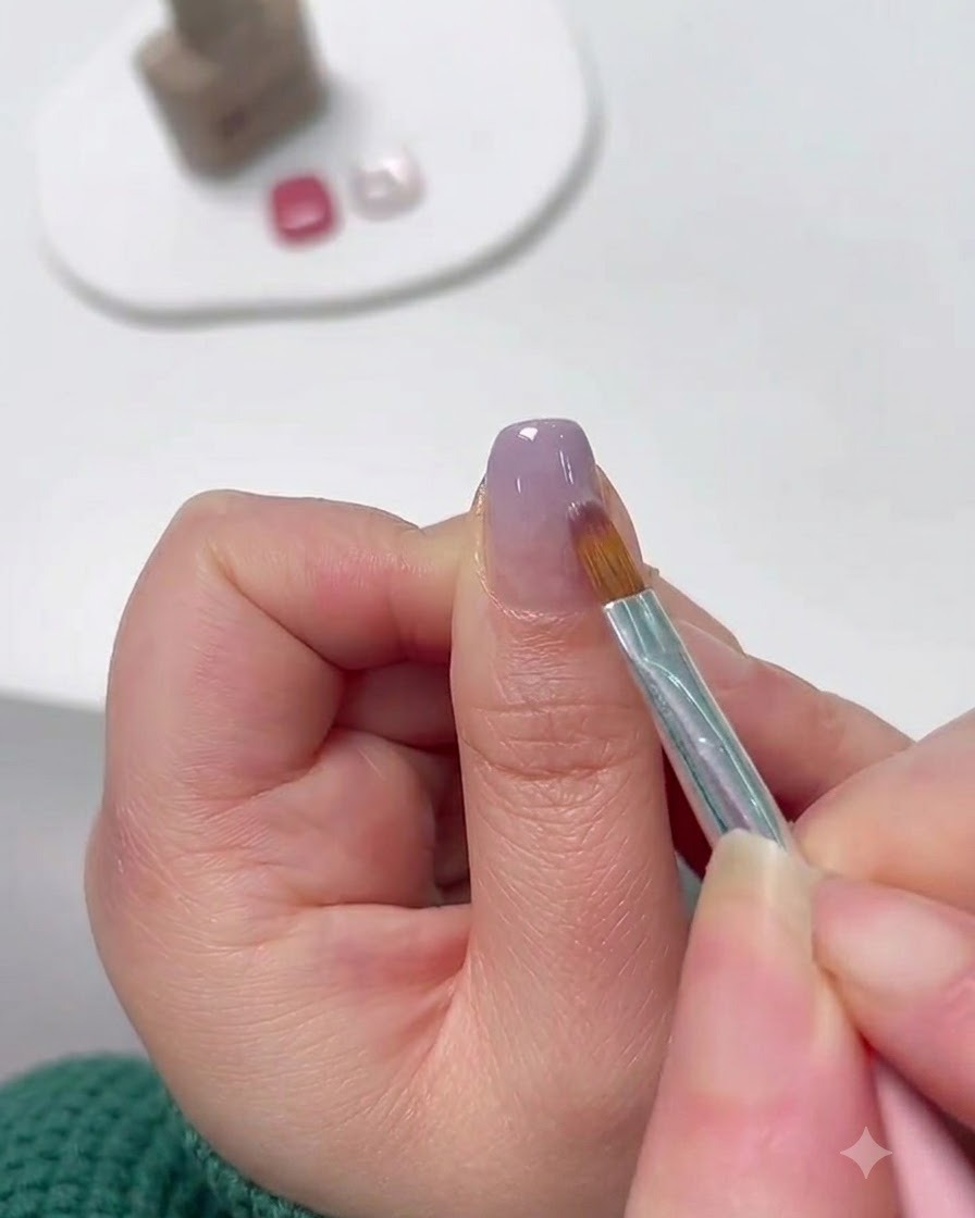 Ein feiner Nail-Art-Pinsel verblendet Lavendel-Gel von der Nagelspitze nach oben, um einen Farbverlauf zu formen.