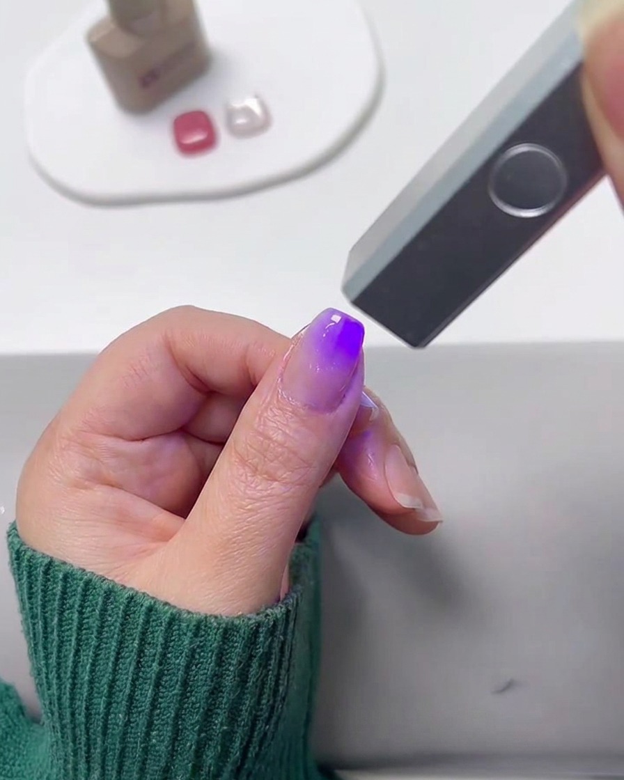 Eine Mini-UV-Lampe härtet einen mit Farbverlauf bemalten Fingernagel aus.
