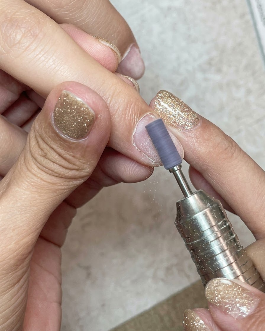 Ein Schleifband auf einem Fräser, das die Oberfläche eines Naturnagels sanft anbuffert.