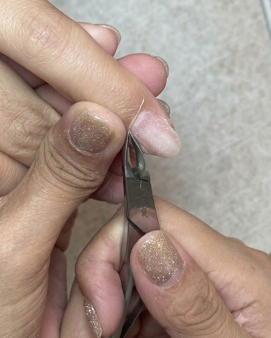 Scharfe Nagelhautschneidezange aus Metall, die präzise einen Streifen abgestorbene Haut vom Nagelhautrand abschneidet.