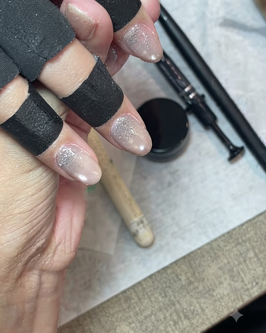 Eine Hand mit schwarzen Fingerschutzhandschuhen, die einen feinen Liner-Pinsel verwendet, um Glitzergel nach unten auf dem Nagel zu verblenden.