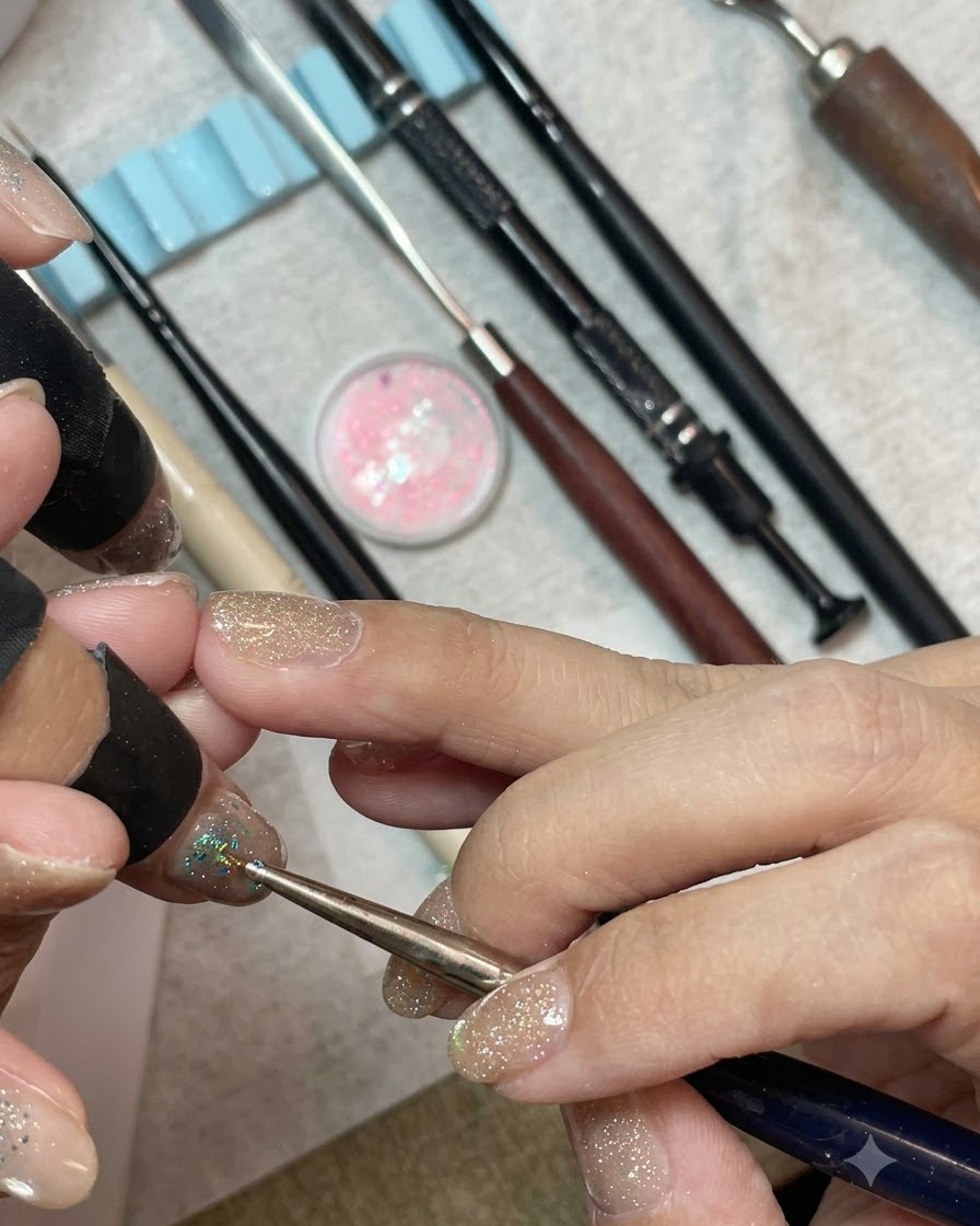 Ein Detailpinsel, der chunky mintblaue und silberne Hexagon-Pailletten dicht auf die Spitze eines mit Gel lackierten Nagels setzt.