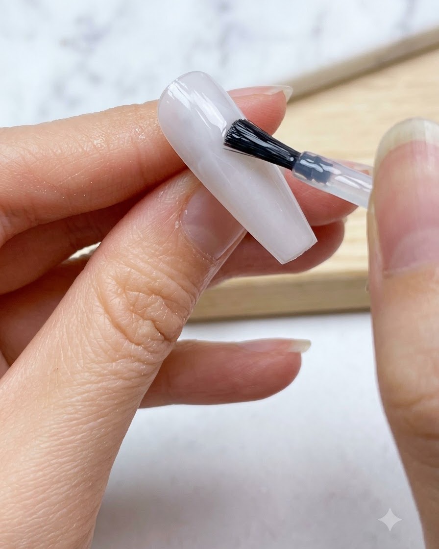 Ein Nagelpinsel trägt eine glatte Schicht durchsichtiges milchig-weißes Gel über die gesamte Nageloberfläche auf.
