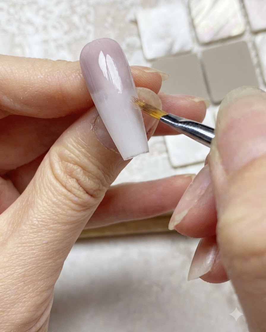 Ein Ombré-Pinsel federt die Kante einer lila Gelschicht auf einer Nude-Nagelverlängerung nach unten ab.