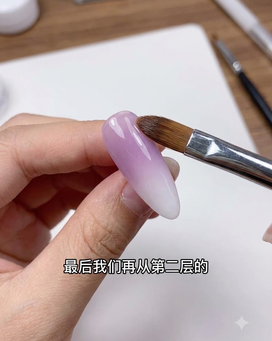 Ein sauberer Nagelpinsel federt sanft die Übergangslinie auf einem lila-weißen Ombré-Nagel ab.