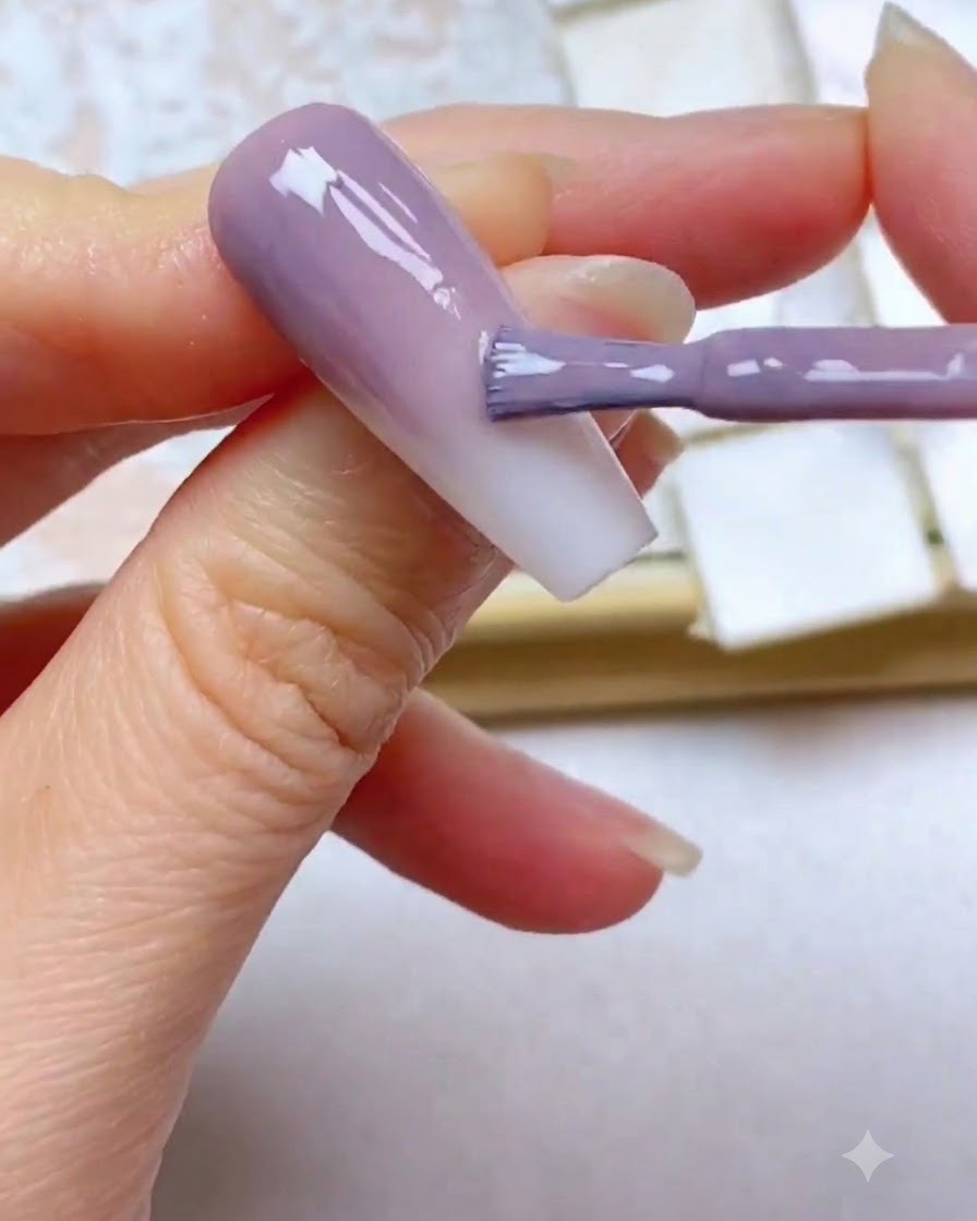 Ein Gelpinsel trägt eine dritte lila Farbschicht nahe dem oberen Nagelrand auf.