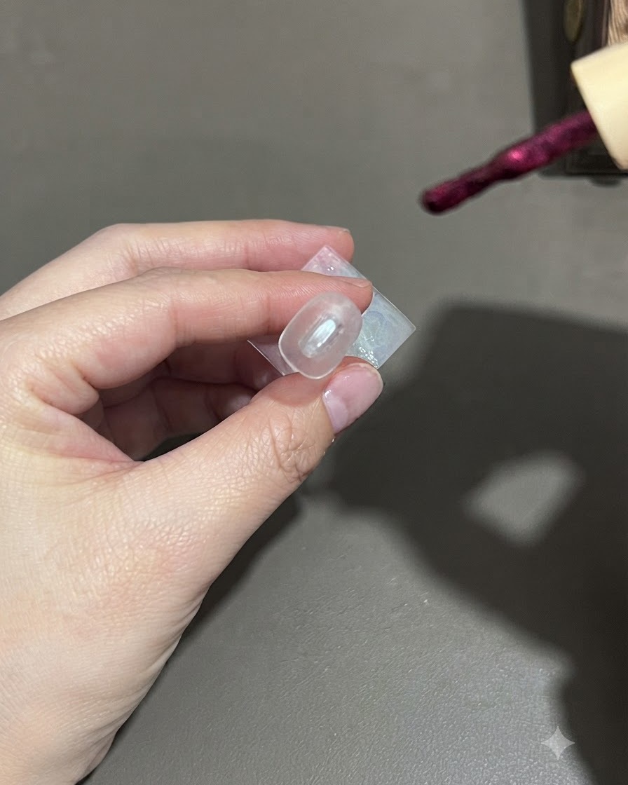 Ein Pinsel trägt dunkles violettes Cat-Eye-Gellack gleichmässig auf einen Nagel auf.
