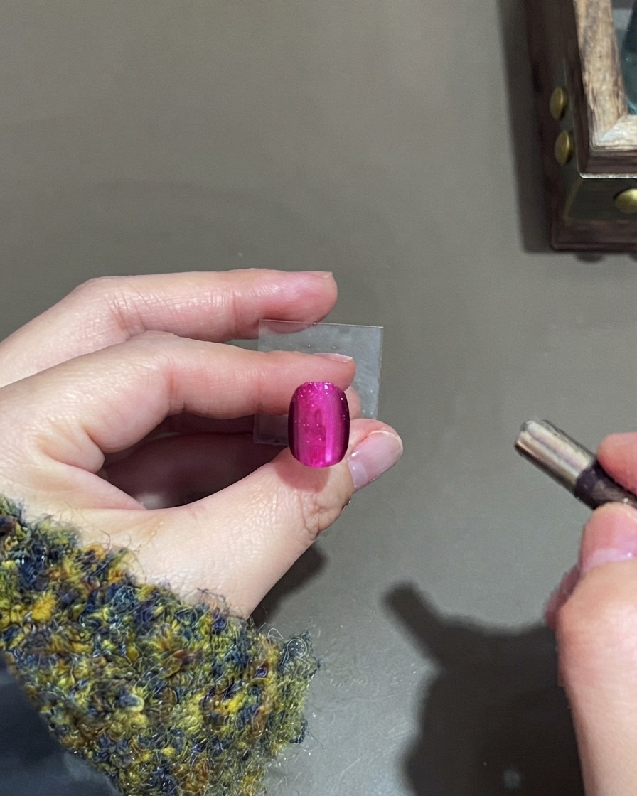 Ein kleiner zylindrischer Magnet schwebt in der Nähe eines pinkfarbenen Cat-Eye-Gelnagels, um das Highlight zu formen.