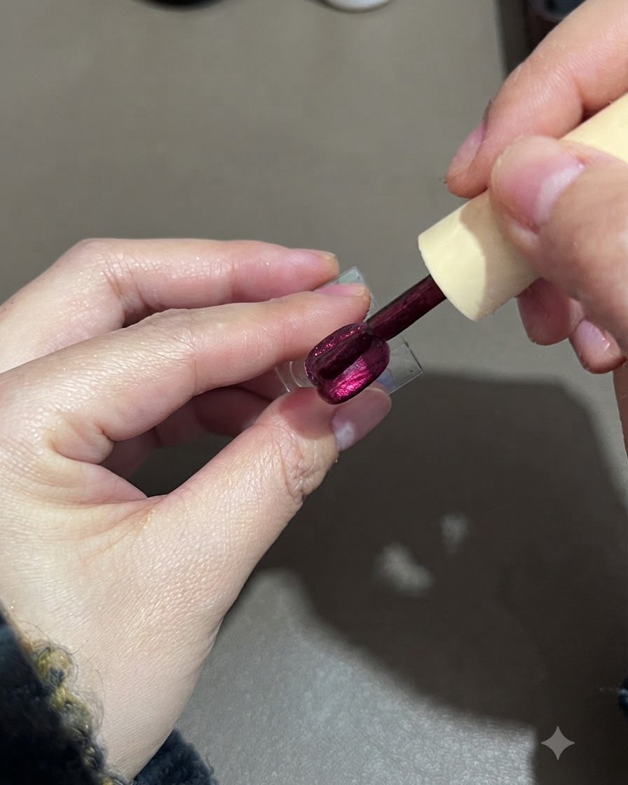 Ein Pinsel glättet eine zweite Schicht violetten Cat-Eye-Gellacks auf einem Nagel-Display-Ständer.