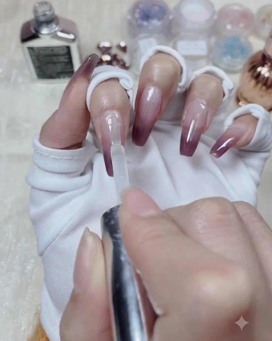 Ein Flaschenpinsel trägt klares Modellagegel über die gesamte Oberfläche eines mit Farbverlauf lackierten Nagels auf.