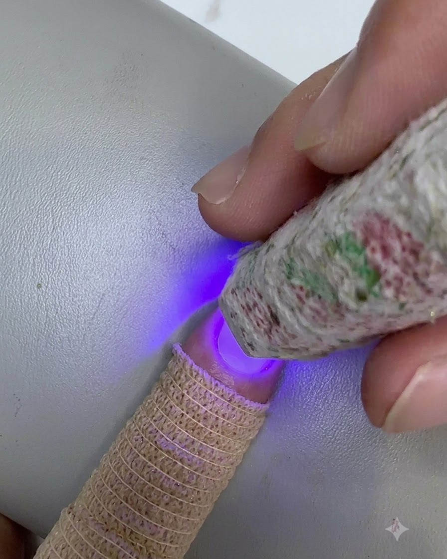 Eine gemusterte Mini-UV/LED-Lampe wird über die Nagelspitze gehalten, um eine verblendete Schicht Klargel auszuhärten.