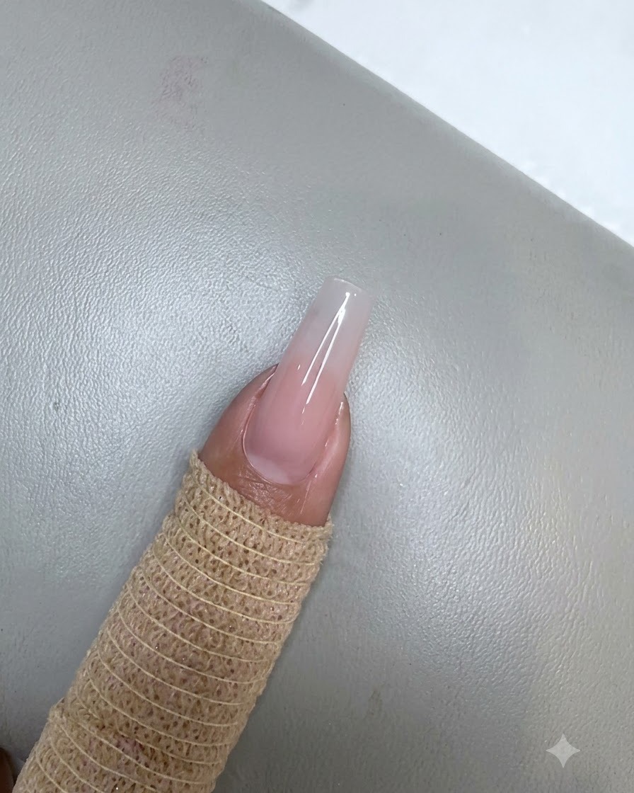 Ein Fingernagel mit einer ausgehärteten Nude-Pink-Gel-Schicht unter einer kleinen lila UV-LED-Lampe.