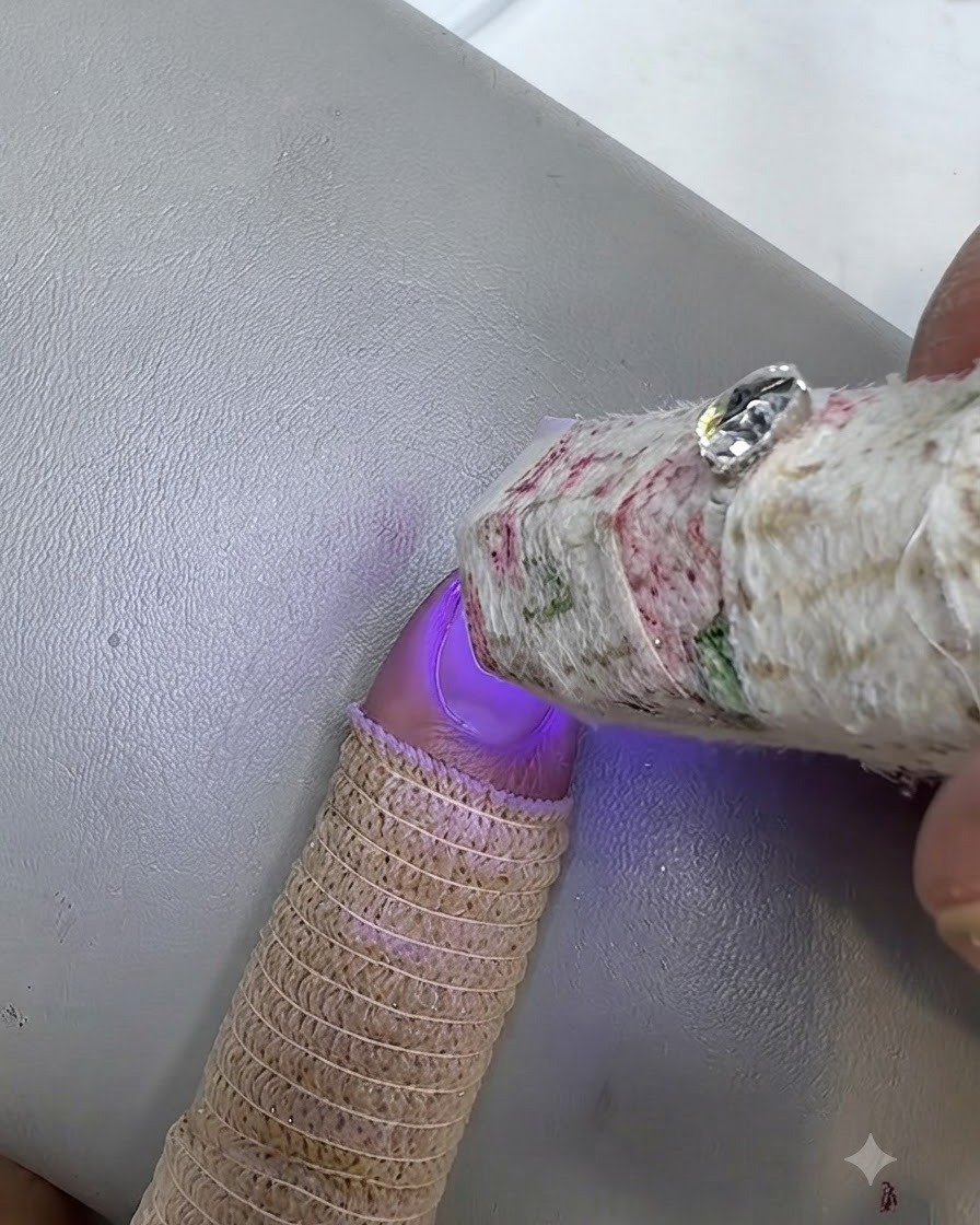Eine kleine UV-Lampe härtet einen bemalten Nagel aus, wobei ein Finger einen Strick-Fingerschutz trägt.