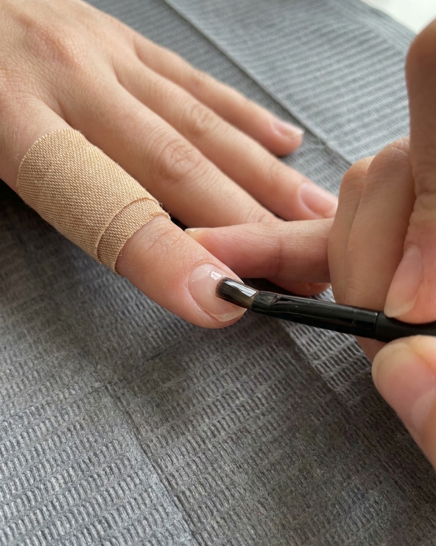 Ein flacher Gelpinsel trägt eine klare Schicht Verstärkungsgel auf den verzierten Nagel auf.