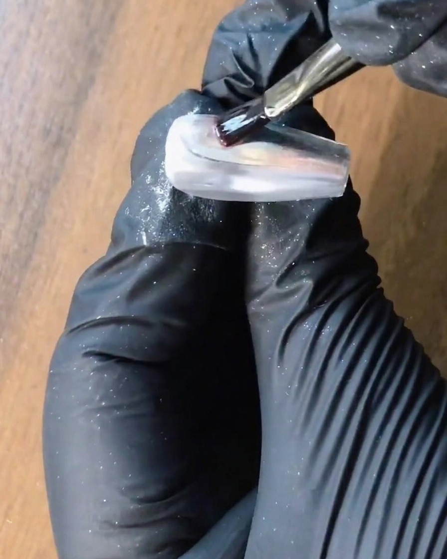 Ein Pinsel trägt klares Verstärkungsgel auf einen silbernen Chromnagel auf.