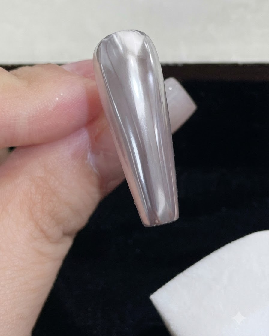 Ein weißer Schaumstoff-Schwammblock wischt überschüssiges Spiegelpuder von einem glänzenden Chromnagel ab.