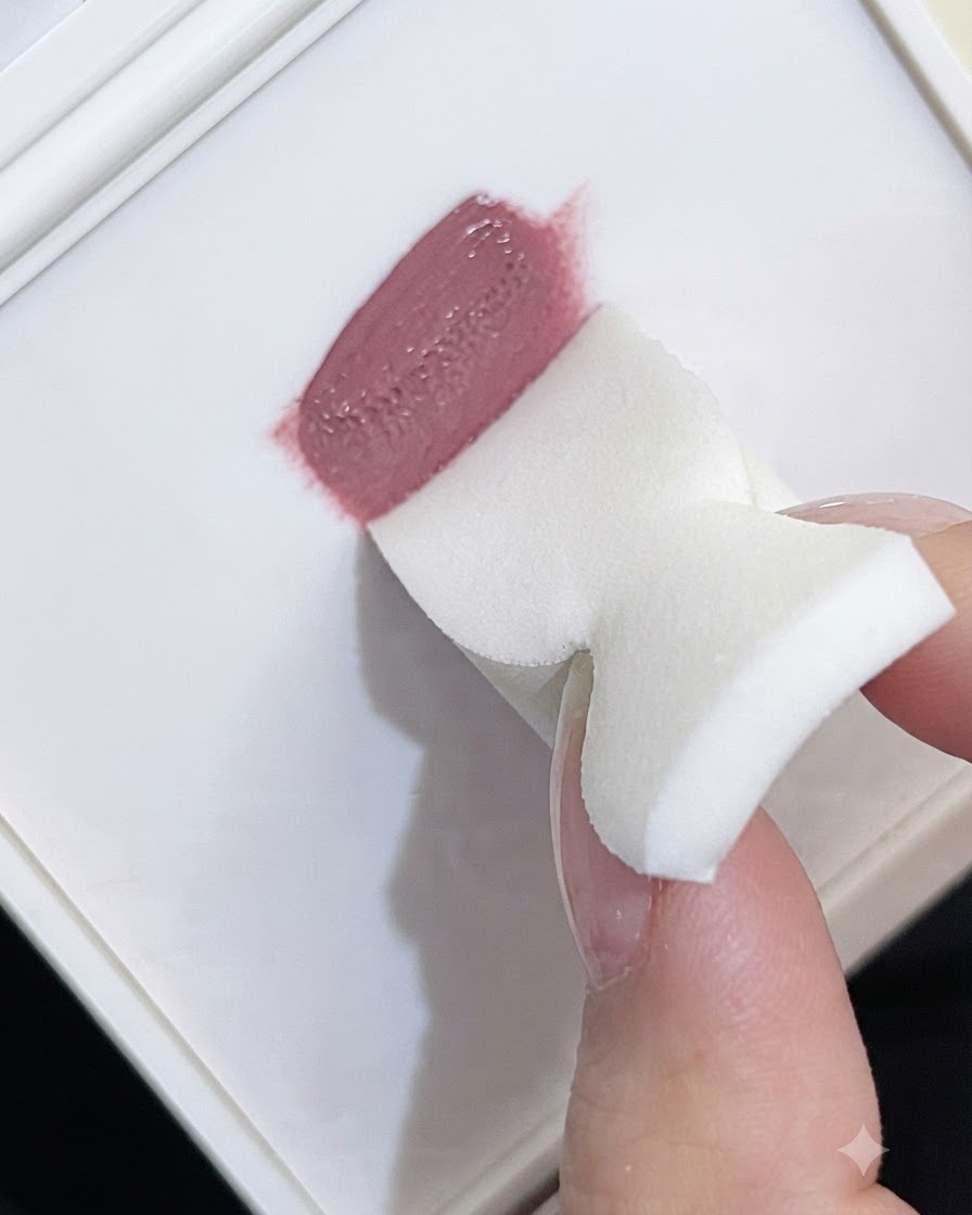 Die Kante eines weißen Schaumstoffschwamms nimmt malvenfarbenes Patting-Gel von einer Palette auf.