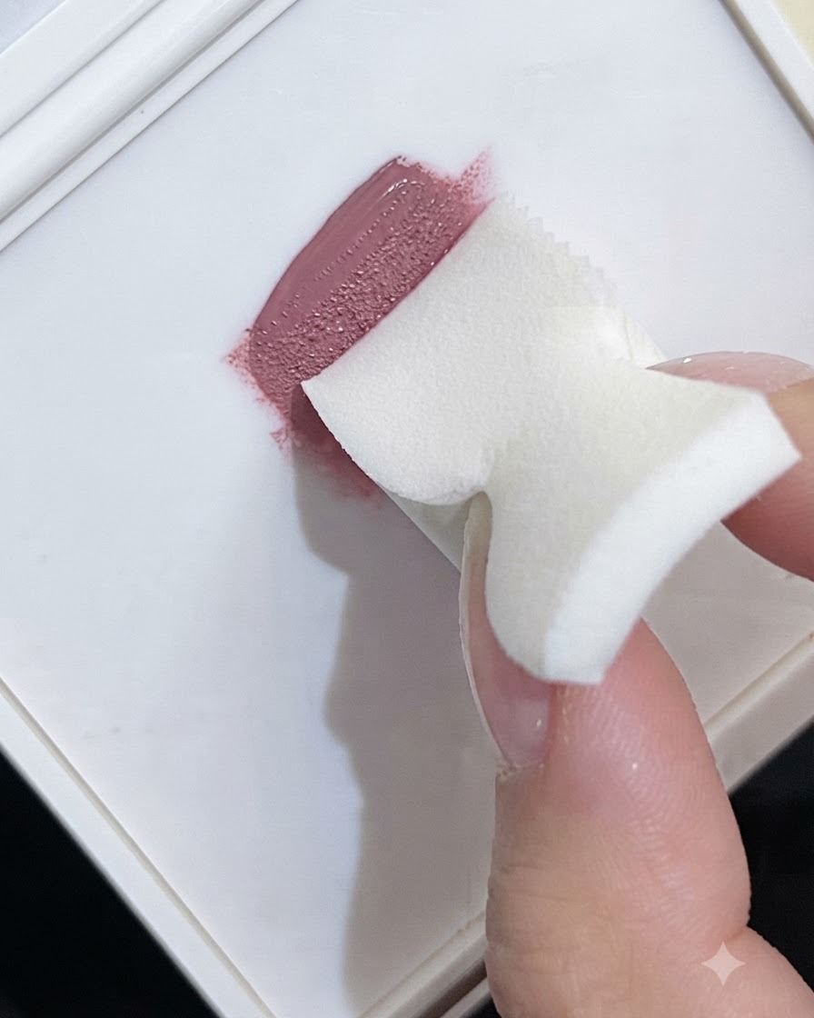 Ein Make-up-Schaumstoffschwamm nimmt rosa Gel-Nagellack von einer weißen Palette auf, um eine Farbverlauf-Textur zu erzeugen.