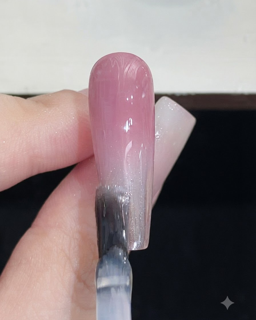 Ein Nagelpinsel trägt einen klaren Topcoat über einen fertigen rosa Verlaufsnagel auf.